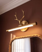 Clérachic brass antler wall light lit warm above a gilt-framed mirror, the angled tube and round backplate seen close up.
