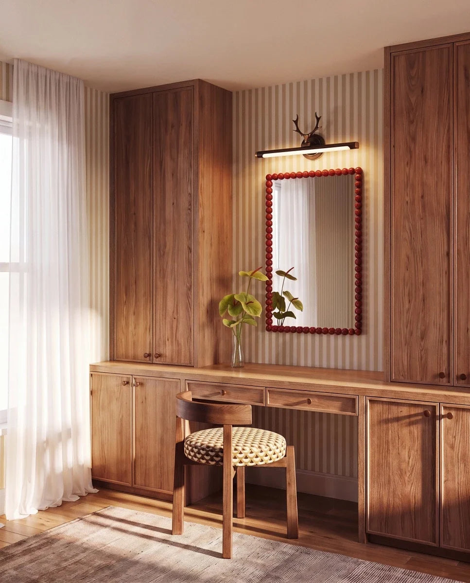 Clérachic black antler wall light lit above a red beaded mirror, over a wooden dressing table and striped wallpaper.