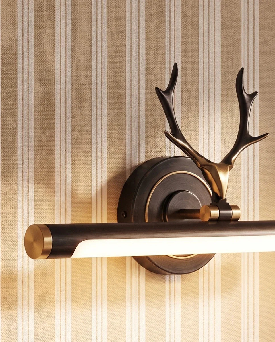 Clérachic close-up of a black and gold antler wall light, its bronze backplate, gold end cap and lit tube against striped wallpaper.