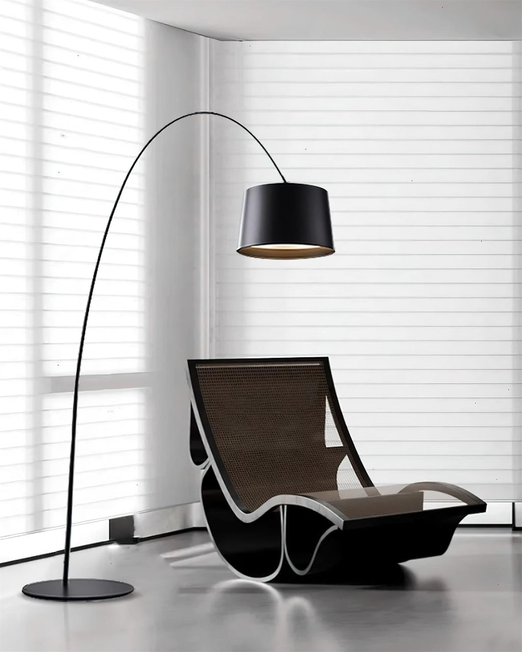 Black Clérachic arc floor lamp beside a black rocking lounger in a corner with white horizontal blinds.