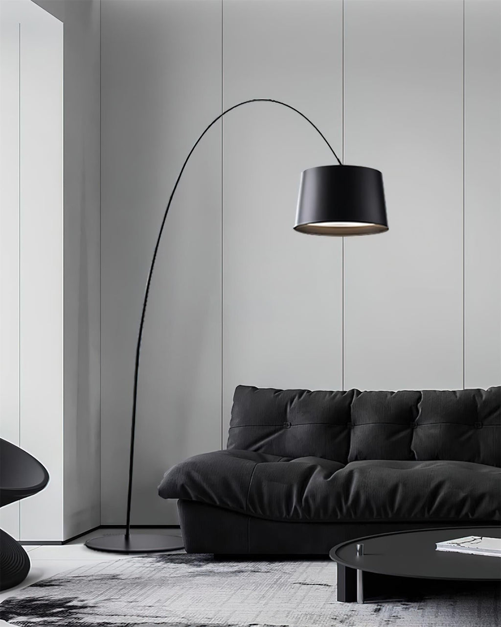 Black Clérachic arc floor lamp with a long thin arm, over a black leather sofa in a grey-panelled room.