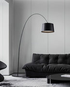 Black Clérachic arc floor lamp with a long thin arm, over a black leather sofa in a grey-panelled room.