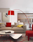 Red Clérachic arc floor lamp over a beige sofa with red cushions, a white coffee table and a red armchair.