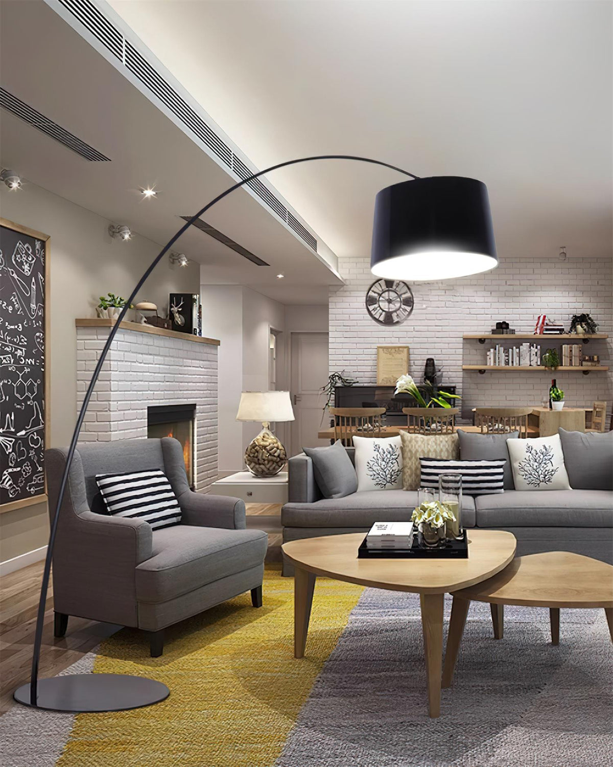 Black Clérachic arc floor lamp over grey armchairs and a wooden coffee table in a living room with a brick wall and yellow rug.