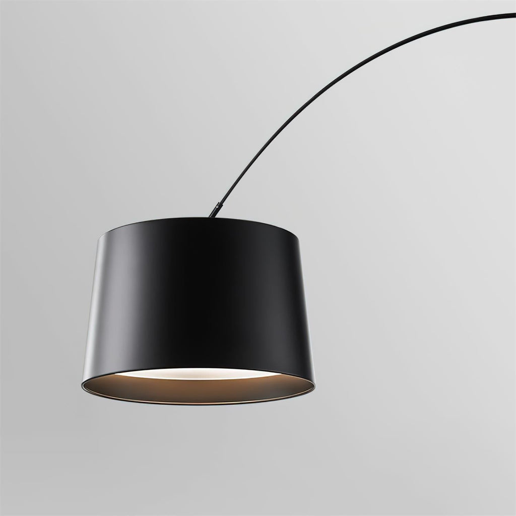 Close view of the black drum shade on this Clérachic arc floor lamp, with a pale glowing underside and the arm curving away.