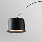 Close view of the black drum shade on this Clérachic arc floor lamp, with a pale glowing underside and the arm curving away.