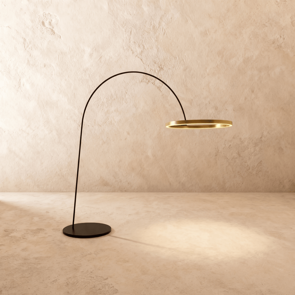 Clérachic arc floor lamp with a thin black arm and a gold ring light, on a round black base against a limewash wall.