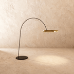 Clérachic arc floor lamp with a thin black arm and a gold ring light, on a round black base against a limewash wall.