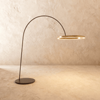 Clérachic taller arc floor lamp with a brushed gold ring and wider black base, glowing warm against a limewash wall.