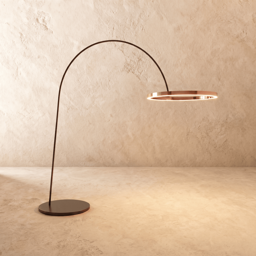 Clérachic taller arc floor lamp with a polished rose gold ring on a black arm, its edge lit with a warm line of light.
