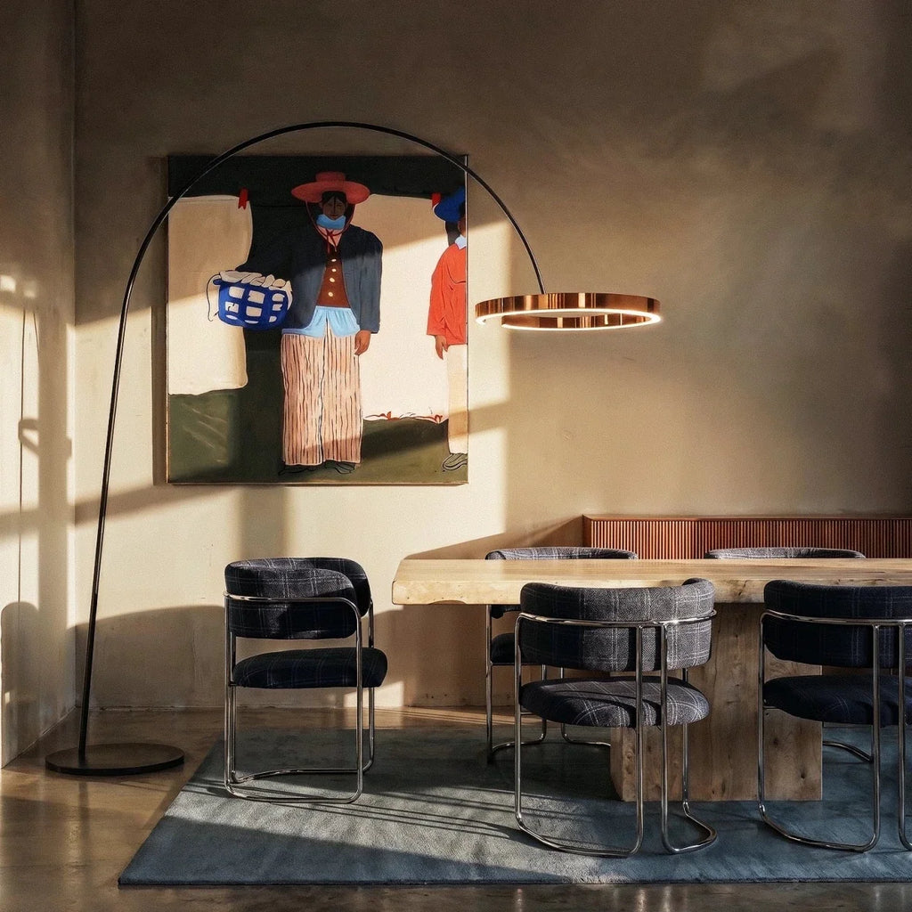 Clérachic arc floor lamp with a rose gold ring reaching over a dining table and grey velvet chairs in warm evening light.