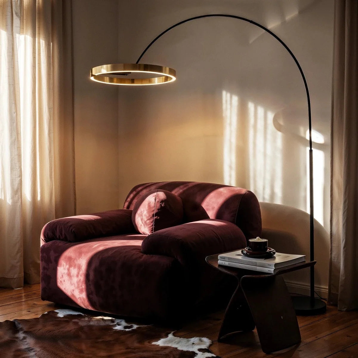 Clérachic arc floor lamp with a gold ring reaching over a burgundy velvet armchair in a corner by sheer curtains.