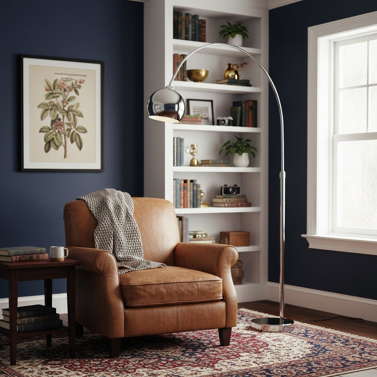Chrome arc floor lamp from Clérachic arching over a tan leather armchair, with built-in shelves and a navy wall behind.