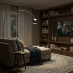 The chrome head of this Clérachic arc lamp hangs over a daybed with a navy throw, beside a shelving unit and television.