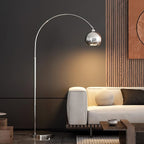 Against a dark panelled wall, this Clérachic chrome arc lamp reaches over a cream sofa and a low wooden table.