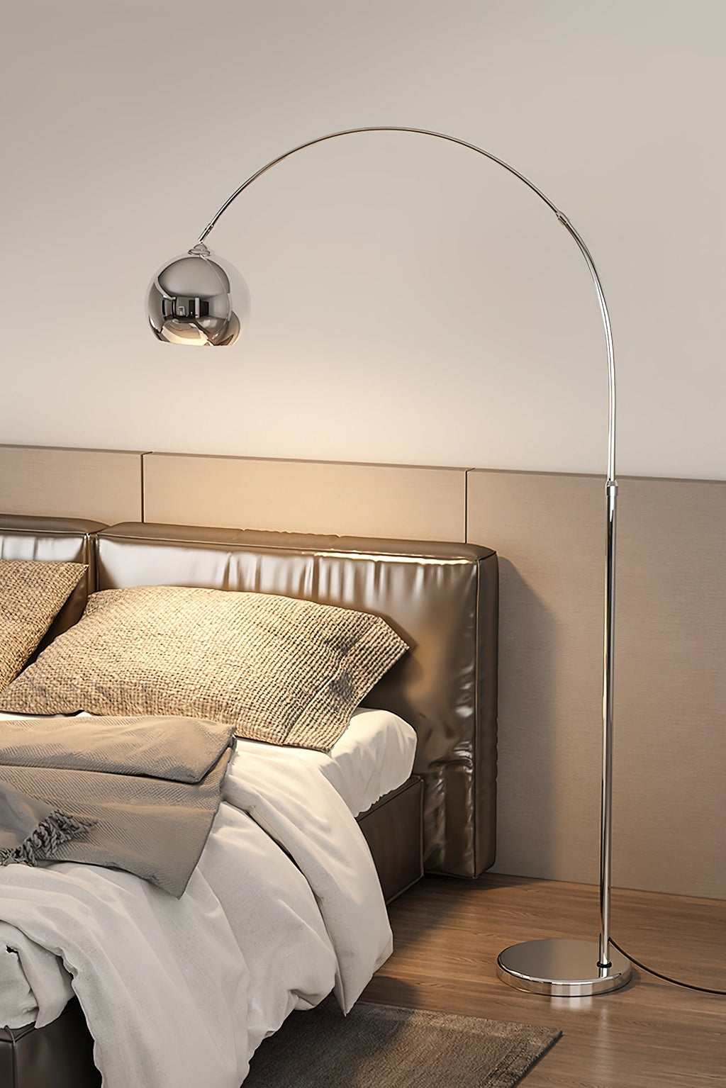 Beside a bed with a quilted leather headboard, a Clérachic chrome arc lamp curves in from the left over a white duvet.