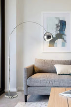 Tall chrome arc lamp from Clérachic over a grey sofa, with an abstract blue and cream painting on the wall behind.