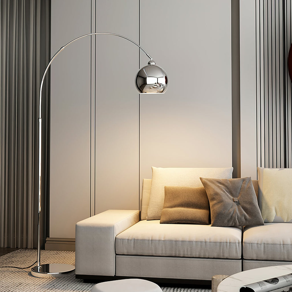 This Clérachic arc lamp's chrome ball head hangs above a cream sofa with taupe cushions, in front of grey curtains.