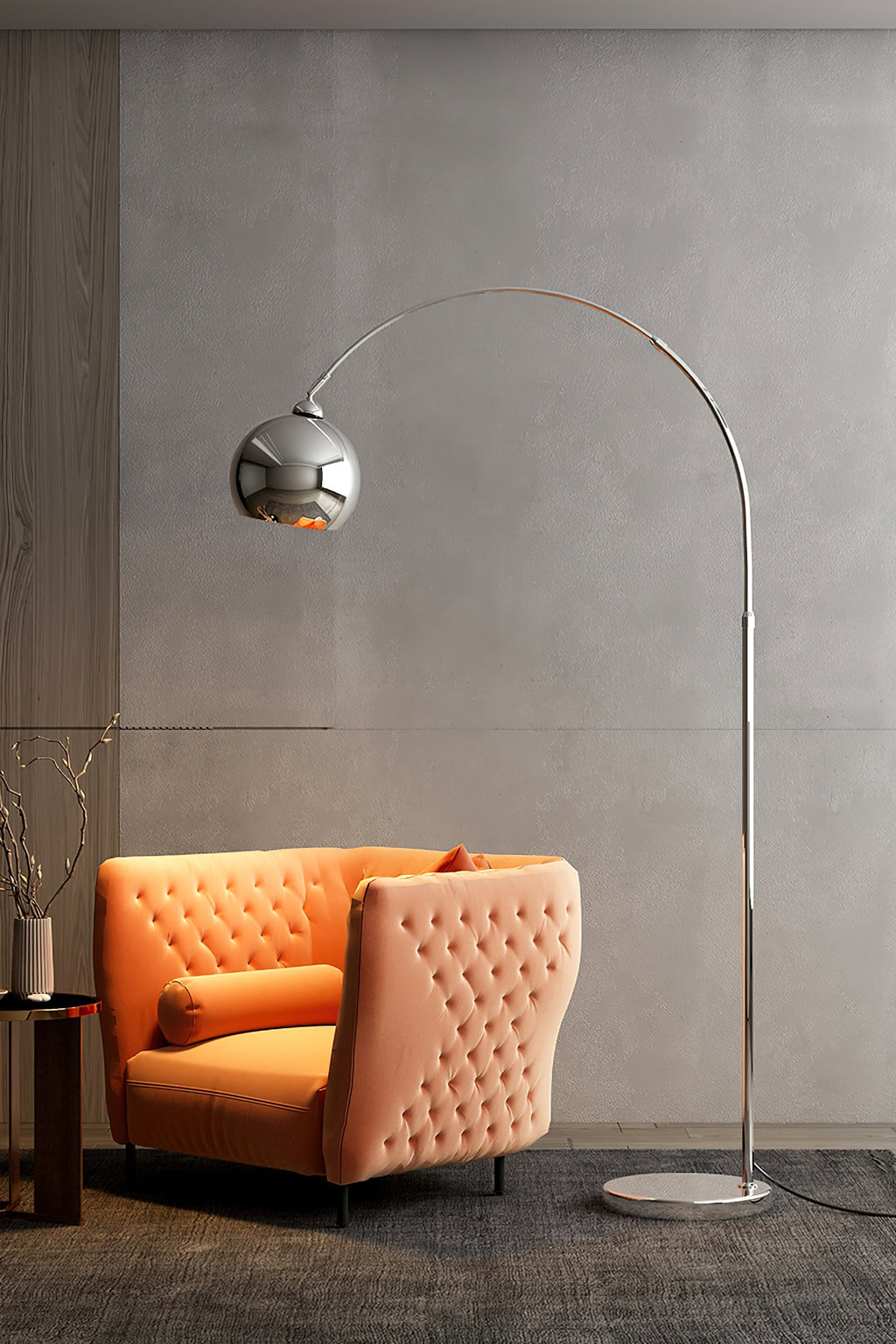 Chrome arc floor lamp from Clérachic beside an orange tufted armchair in a room with a concrete-look grey wall.