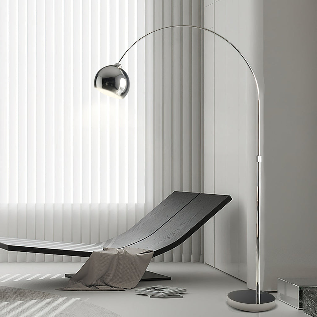 A Clérachic arc lamp curves over a dark lounger with a grey throw, in front of white vertical blinds.