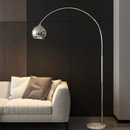 Against a dark wood-slat wall, this Clérachic chrome arc lamp rises behind a cream sofa with a brown cushion.