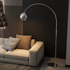 A Clérachic chrome arc lamp curves over a cream sofa with a houndstooth cushion and a brown pillow, with a dark wall behind.