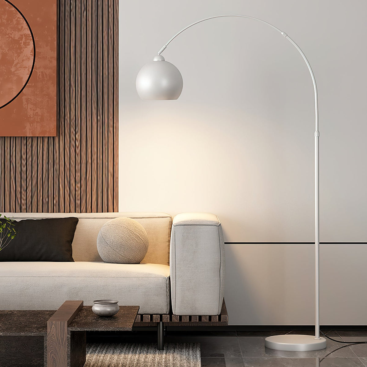White arc floor lamp from Clérachic throwing a warm wash of light on the wall above a cream sofa and a dark coffee table.
