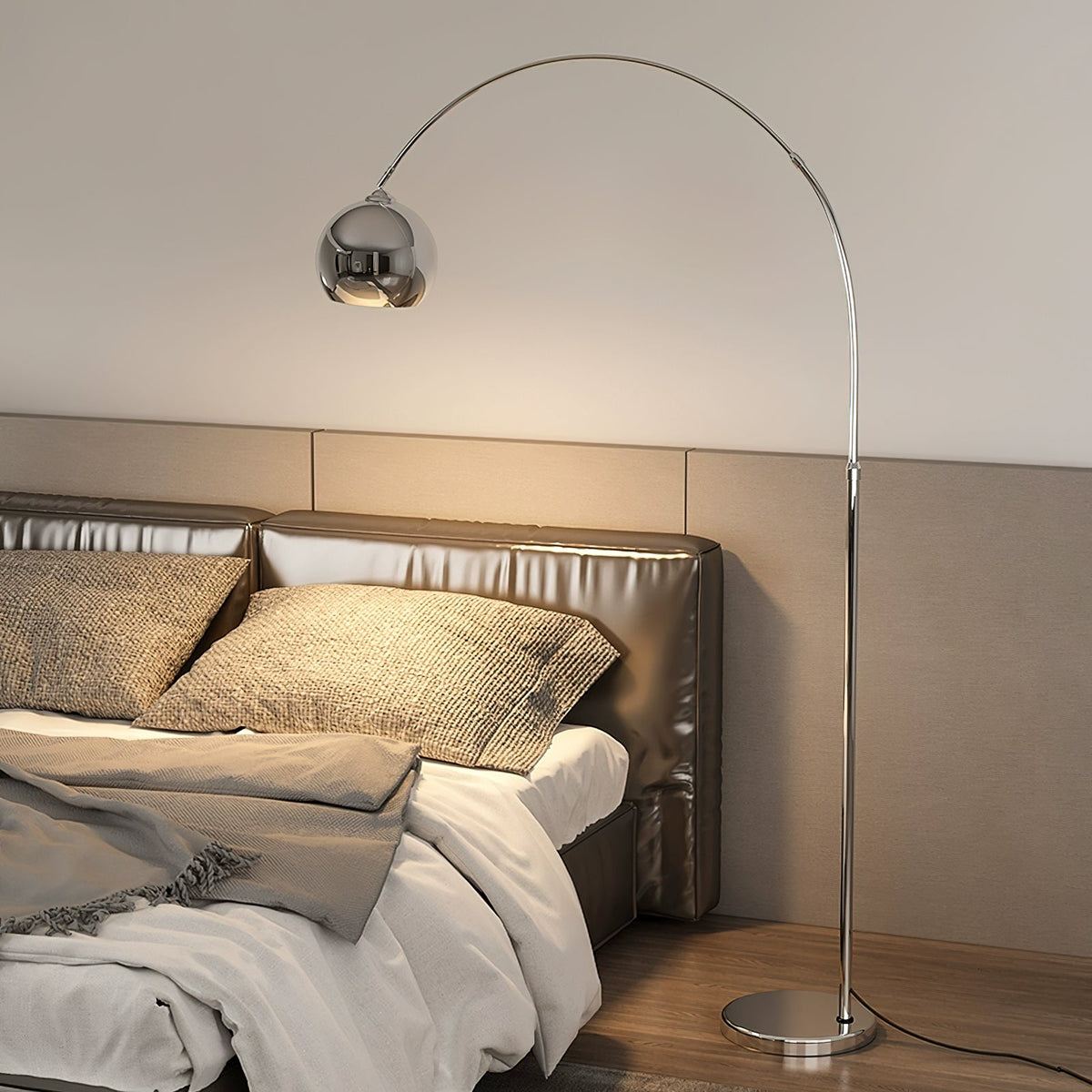Close to a bed with white and grey linen, this Clérachic chrome arc lamp curves in above a leather headboard.