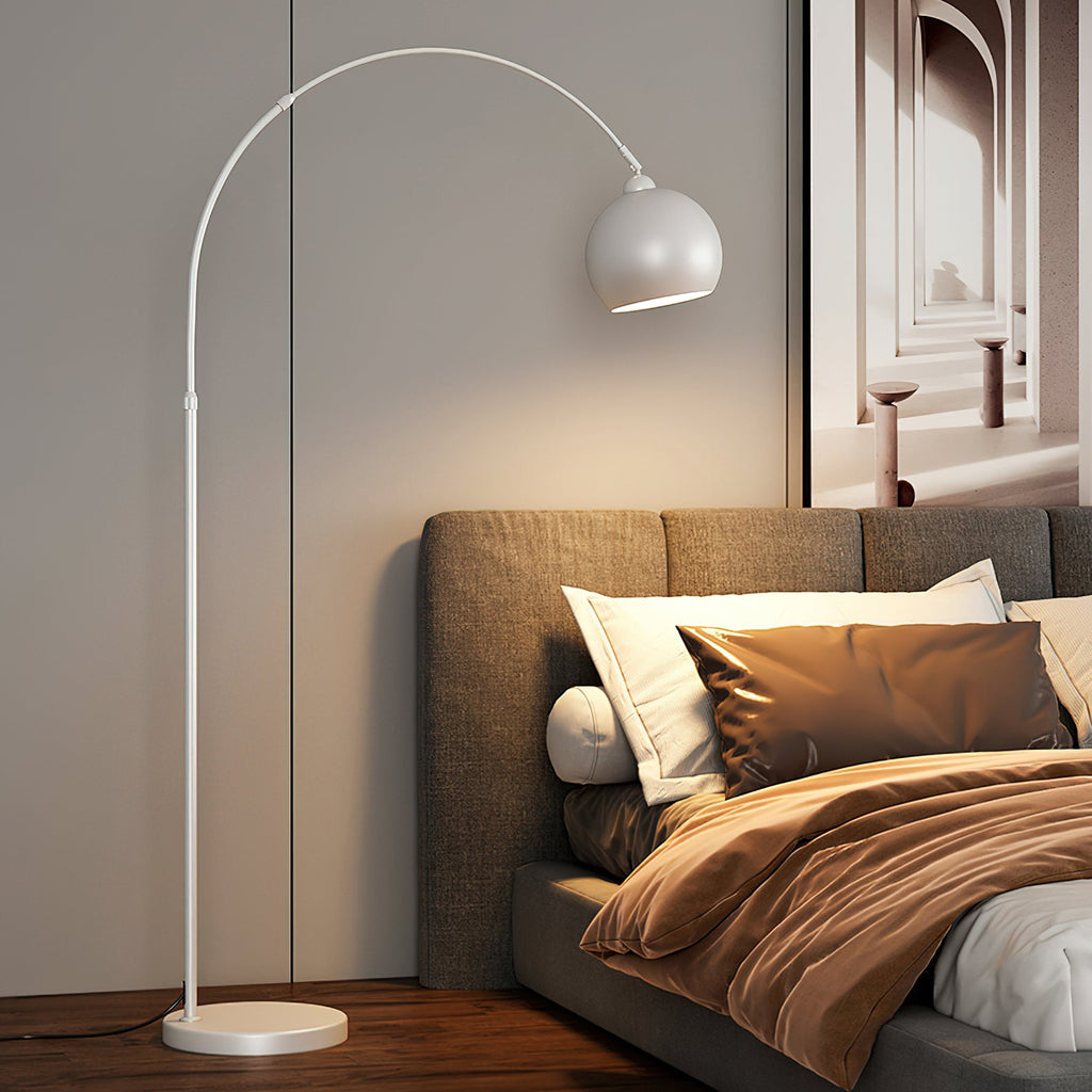 White arc floor lamp from Clérachic with a matte round head and a white base, beside a bed with brown bedding.