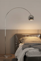 A Clérachic chrome arc lamp stands beside a leather-headed bed, its round head casting a warm glow on the wall.