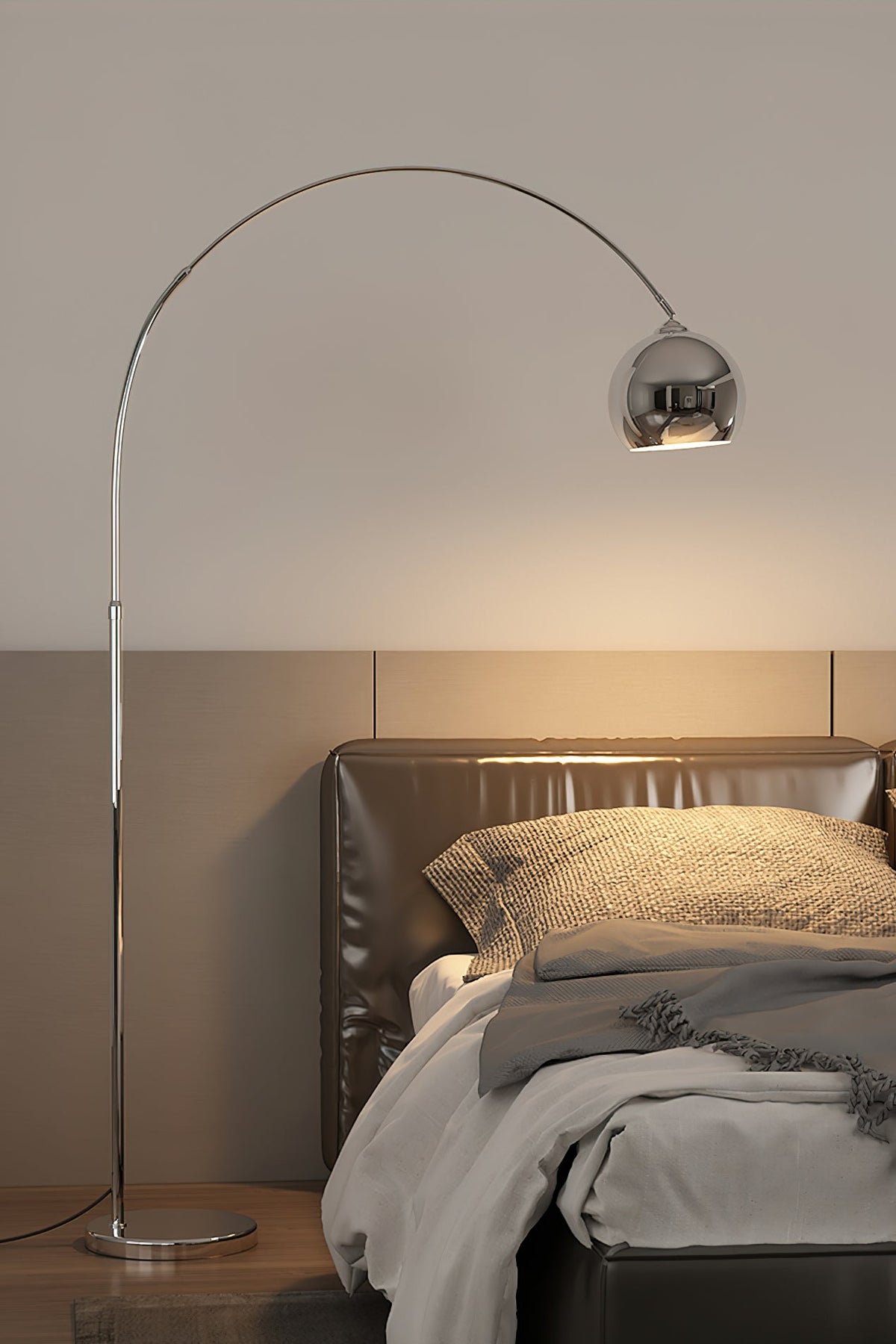 A Clérachic chrome arc lamp stands beside a leather-headed bed, its round head casting a warm glow on the wall.
