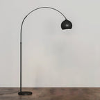 Black arc floor lamp from Clérachic with a matte dome head and a round black base, on a wooden floor against a pale wall.