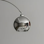 Close view of the mirror-polished chrome ball head on this Clérachic arc lamp, reflecting a room.