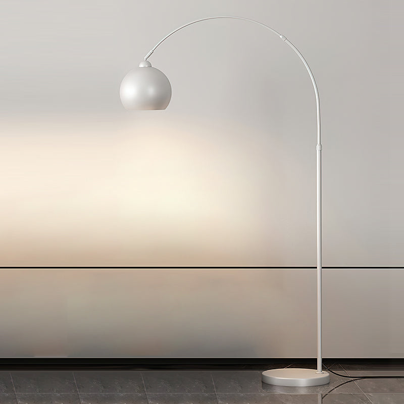 A white Clérachic arc floor lamp with a matte round head and a white base casts light on a pale wall in a minimal room.