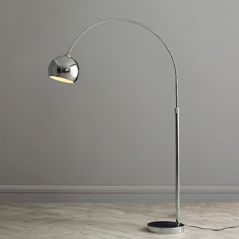 A Clérachic chrome arc lamp with a dark base stands on pale herringbone flooring against a grey wall.