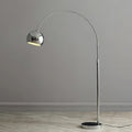 A Clérachic chrome arc lamp with a dark base stands on pale herringbone flooring against a grey wall.