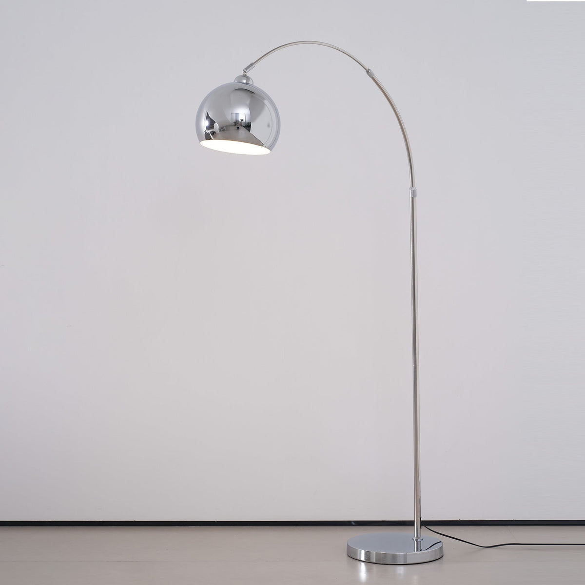 Chrome arc floor lamp from Clérachic, its ball head open to a white inside, on a light grey background.