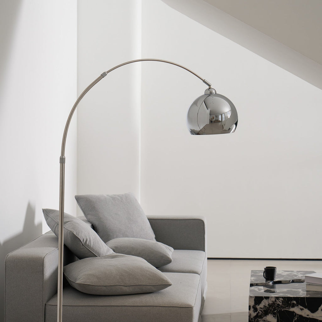 A Clérachic chrome arc lamp reaches over a grey sofa and a black and white marble coffee table.