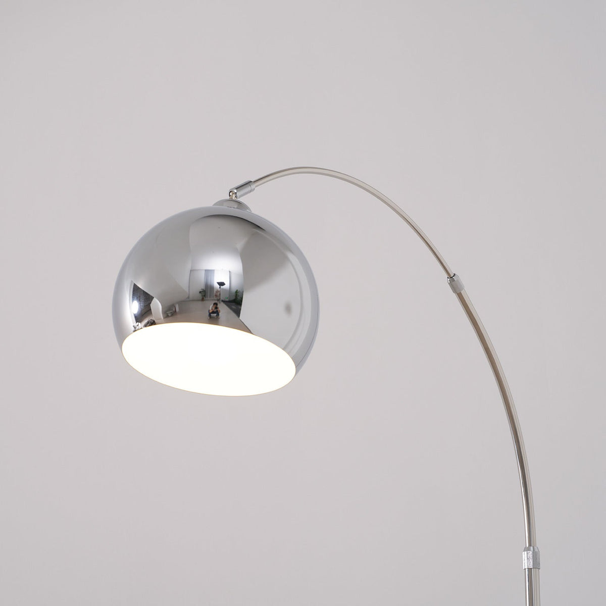 Close view of the round chrome head on this Clérachic arc lamp, with a white inner shade and the arm curving away.
