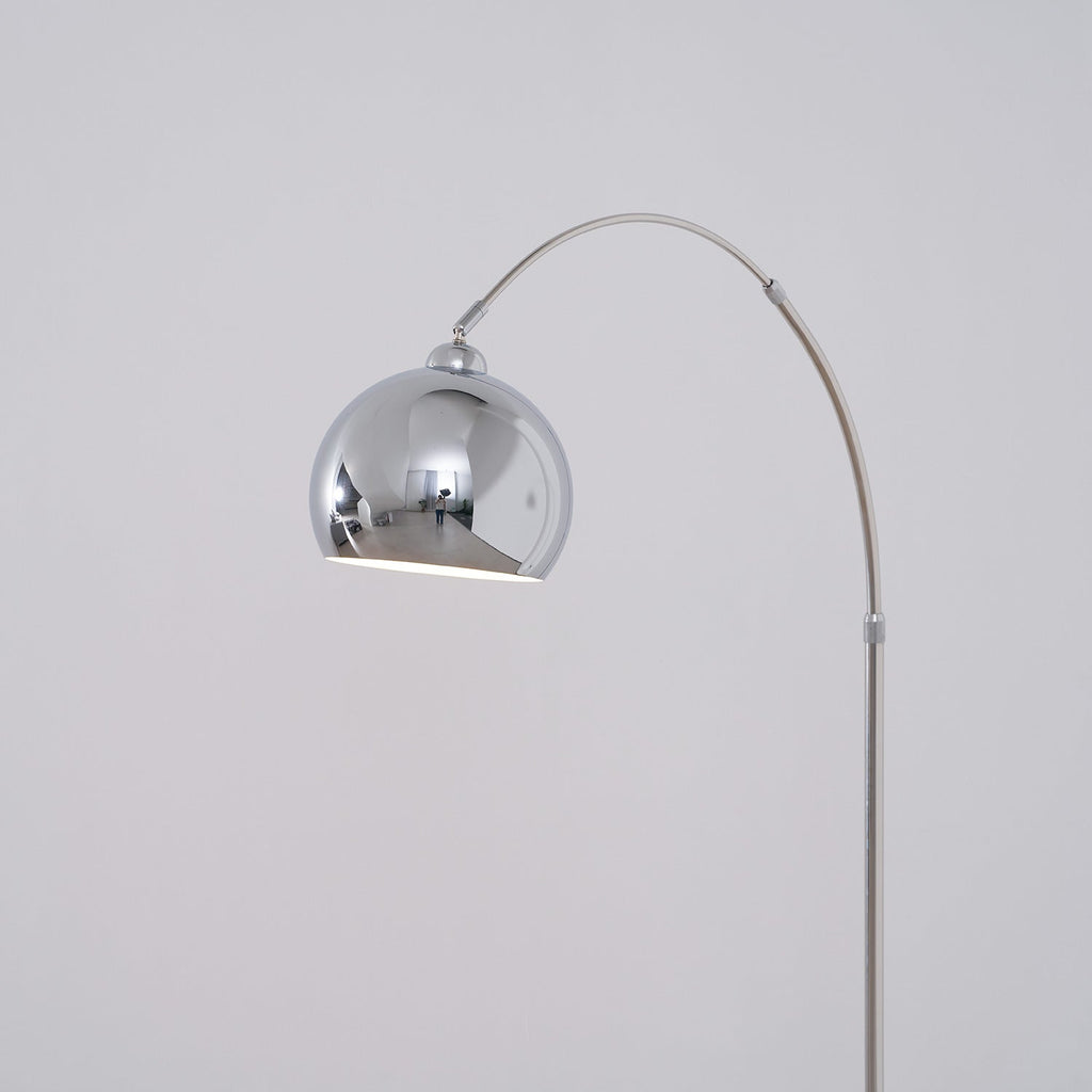 The chrome ball head of this Clérachic arc lamp hangs from the arm, showing its white interior against a soft grey wall.