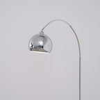 The chrome ball head of this Clérachic arc lamp hangs from the arm, showing its white interior against a soft grey wall.