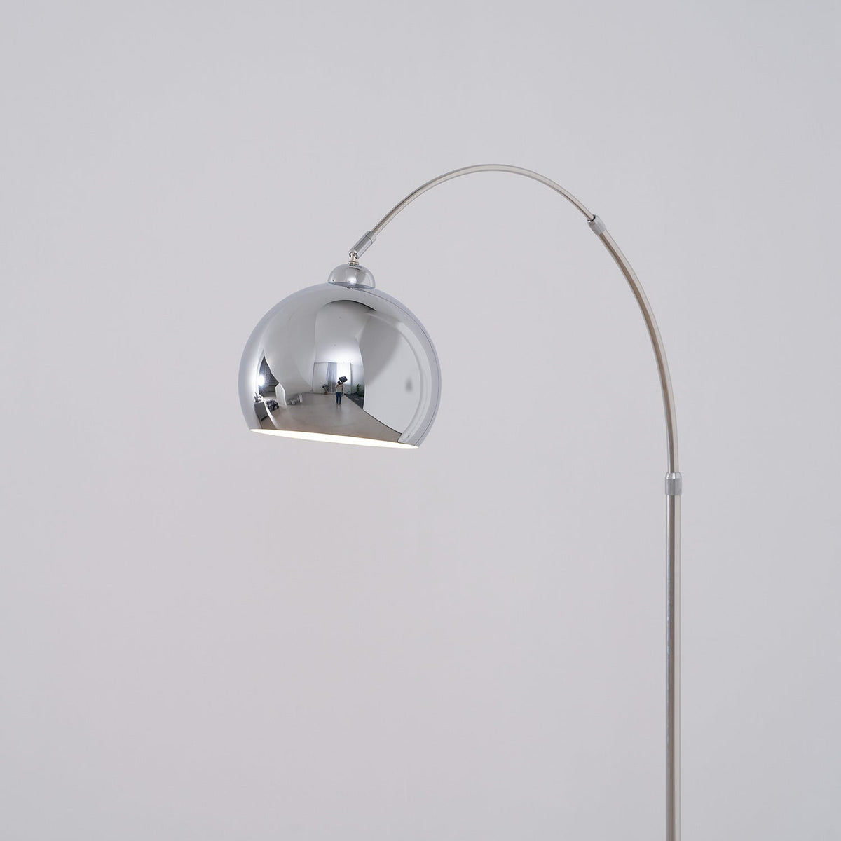 The chrome ball head of this Clérachic arc lamp hangs from the arm, showing its white interior against a soft grey wall.