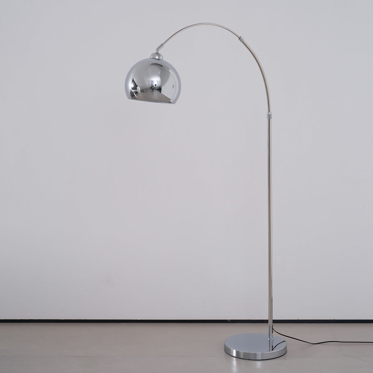 A Clérachic chrome arc floor lamp with a round base and a black cord, on a pale grey background.