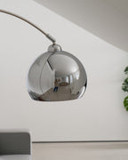 Close view of this Clérachic chrome lamp head from below, with the arm joint on top and a grey sofa blurred behind.