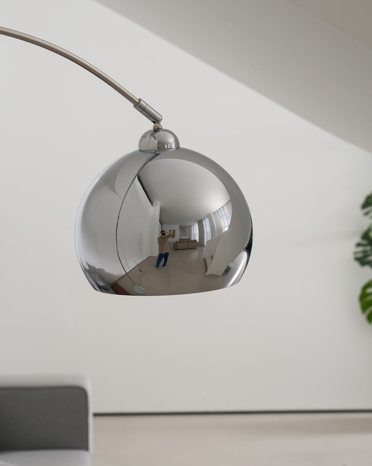 Close view of this Clérachic chrome lamp head from below, with the arm joint on top and a grey sofa blurred behind.