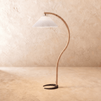 Clérachic arched floor lamp with a bent light-wood stem, black horseshoe base and a white pleated shade on limewash.