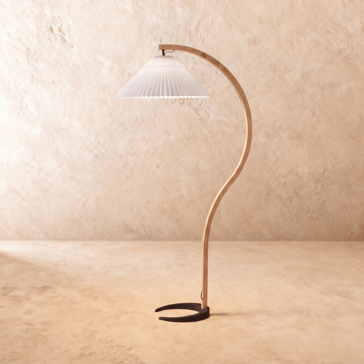 Clérachic arched floor lamp with a bent light-wood stem, black horseshoe base and a white pleated shade on limewash.