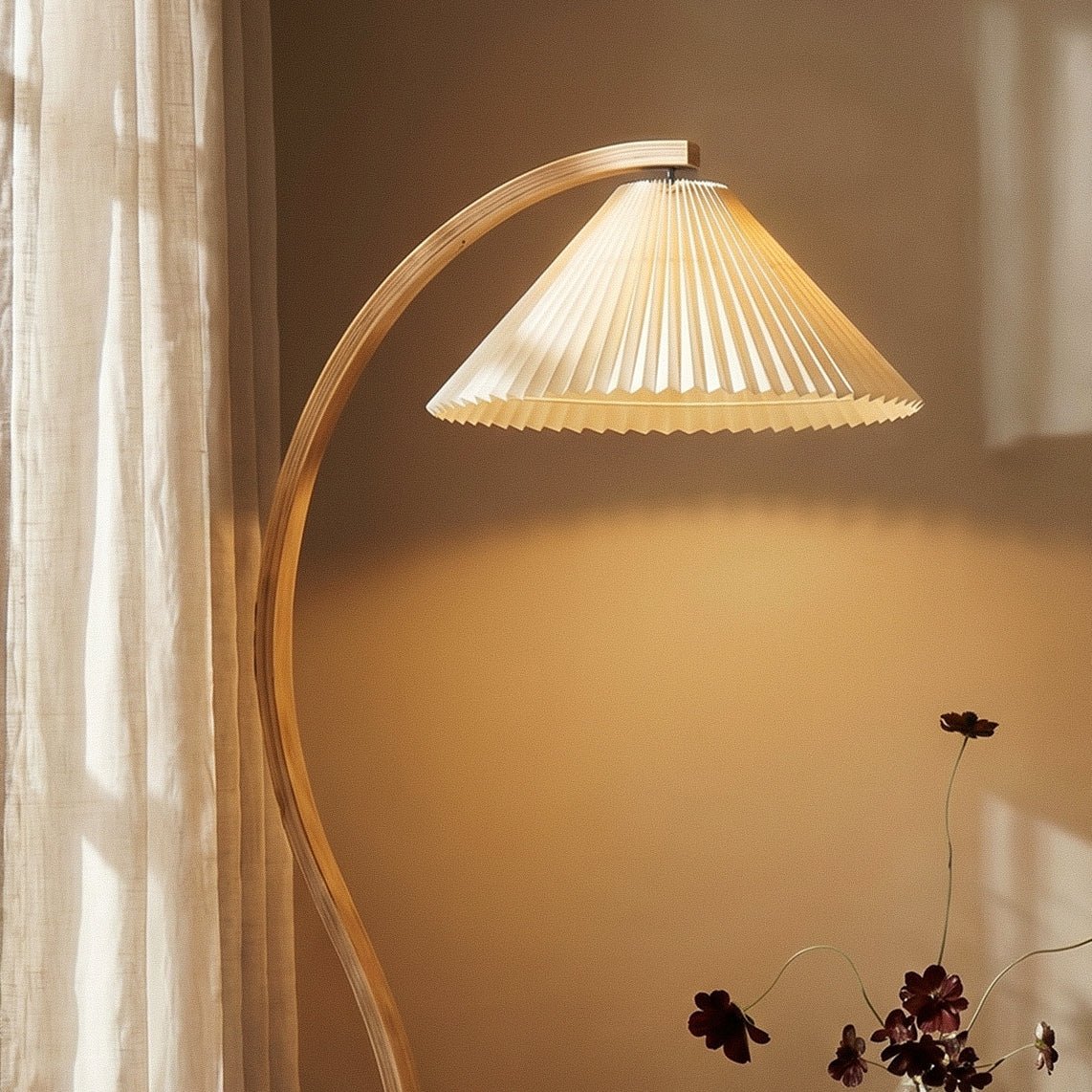 Clérachic floor lamp's cream pleated shade and curved wood stem casting warm light on a wall, beside a sheer curtain.