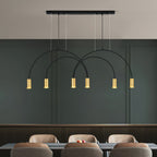 Six brass spot heads glow under the crossing black arches of this Clérachic pendant, in front of a deep green wall and tan dining chairs.