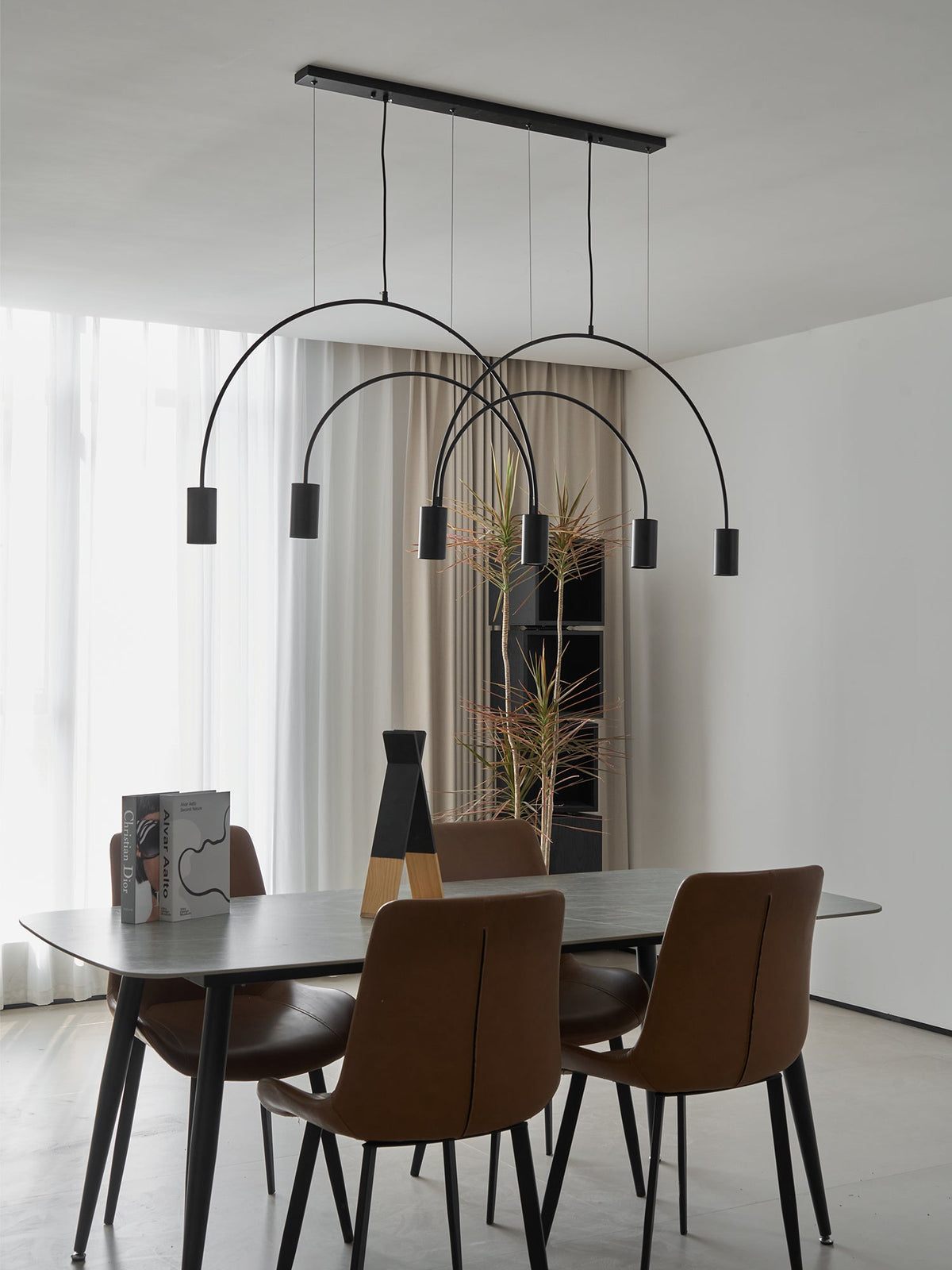 A black Clérachic arch pendant with six spot heads hangs over a dark dining table and brown leather chairs in a bright white room.